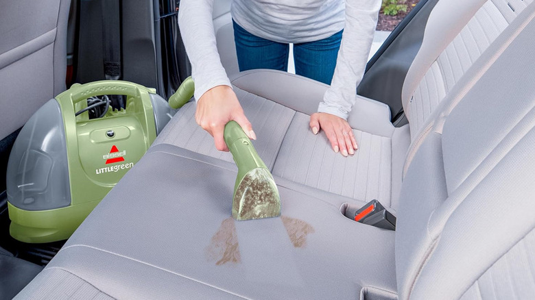 woman using Bissell Little Green upholstery cleaner on car back seat stain