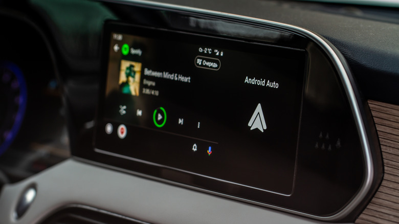 A car's infotainment screen running Android Auto and playing music.