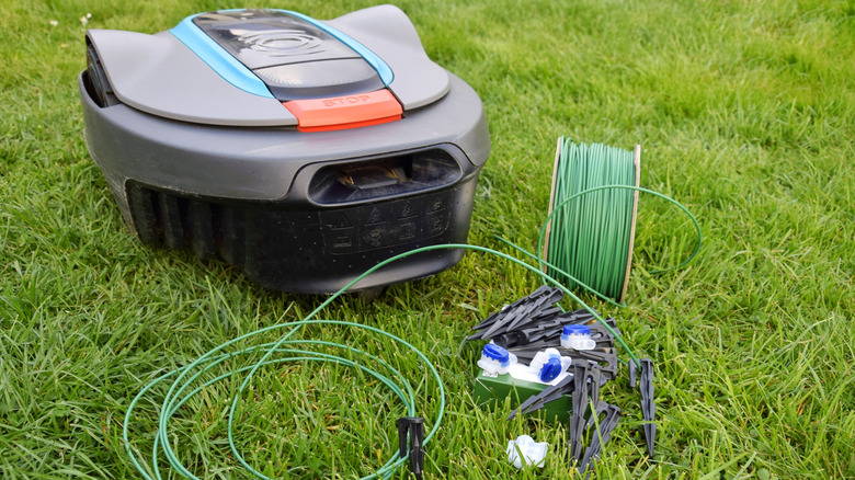 A robot lawn mower on grass next to boundary wires and pegs