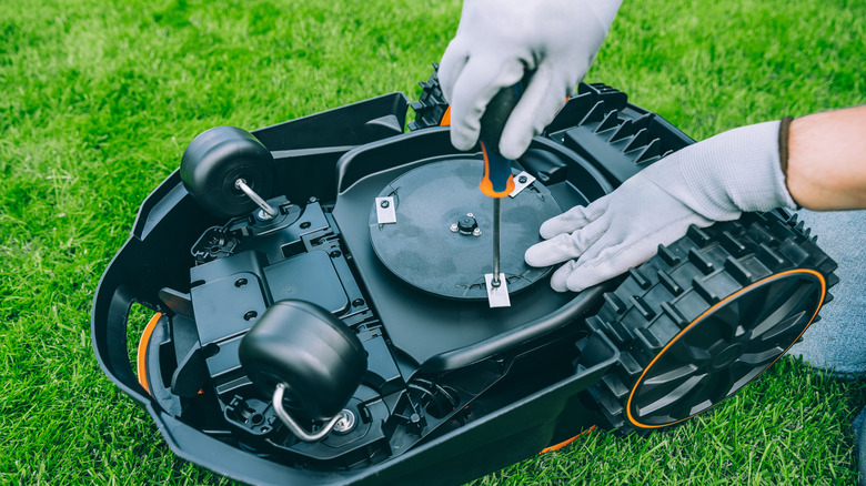 Two gloved hands perform maintenance on a robot lawn mower