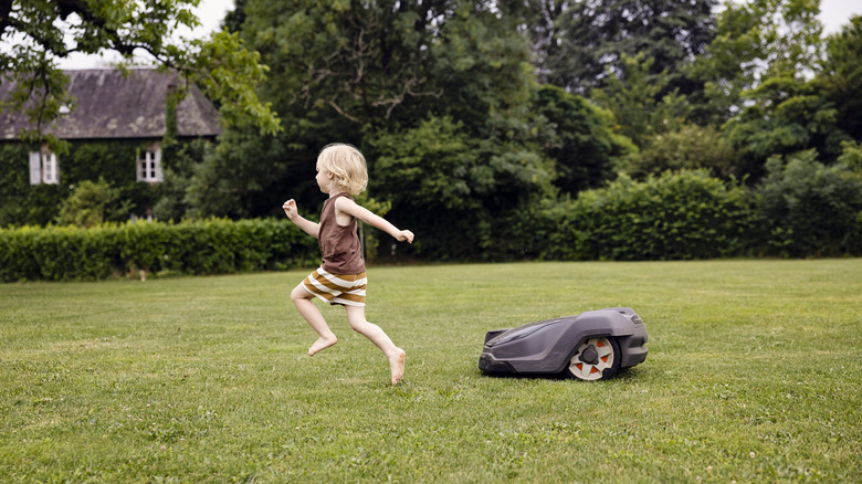 A child running in a yard, followed by a robot lawn mower