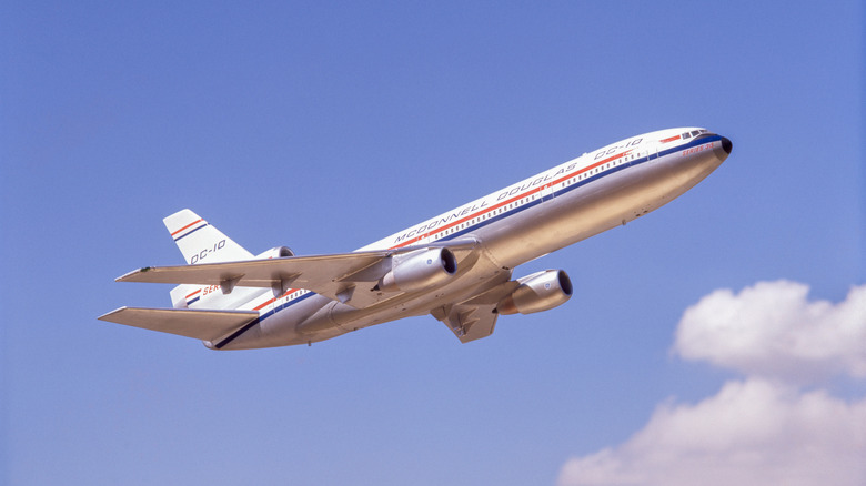 A silver DC-10 airplane flying in a bright blue sky with fluffy white clouds