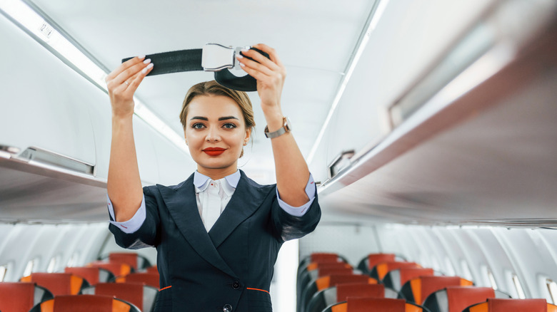 A young, female flight attendant performing a safety briefing on board an empty airplane