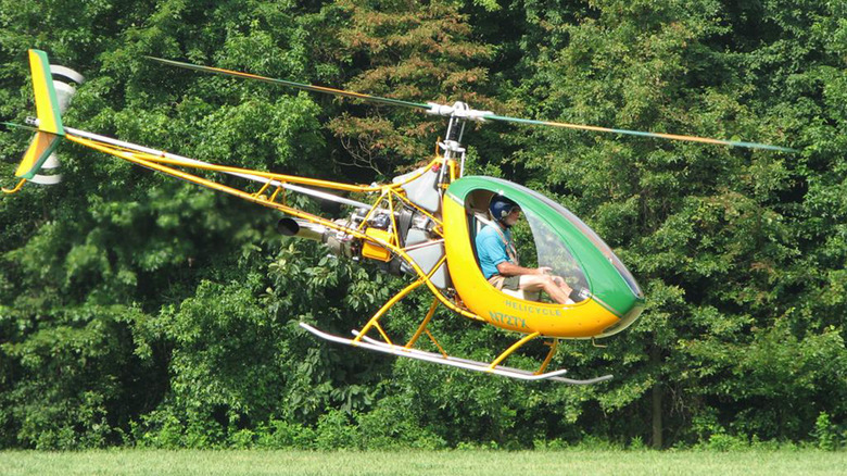 A green and yellow Helicycle helicopter landing in a field