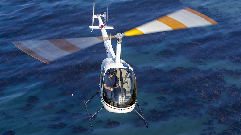 A person flying a Robinson R22 helicopter over water