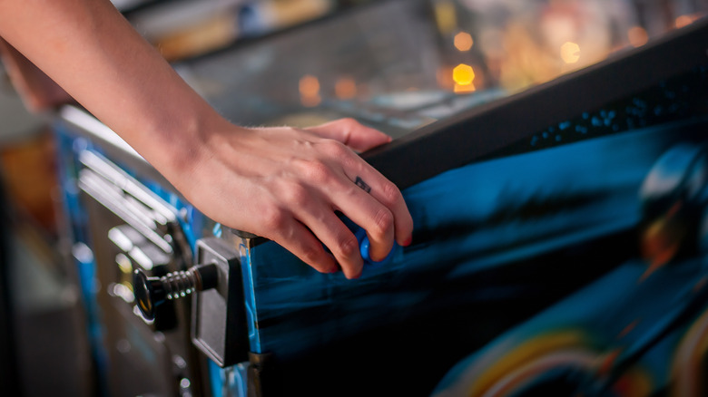 Hand of female pressing button and playing pinball machine