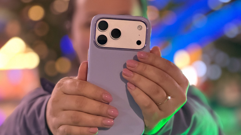 A woman is holding up an iPhone 17 Pro Max in a case against a blurred backdrop