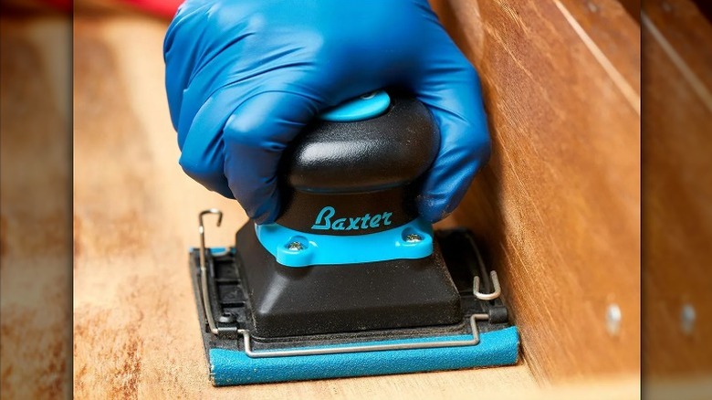 Working with a blue and black air sander on wood.