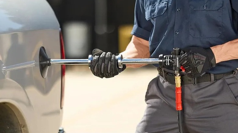 Man using a dent puller tool on a silver vehicle.
