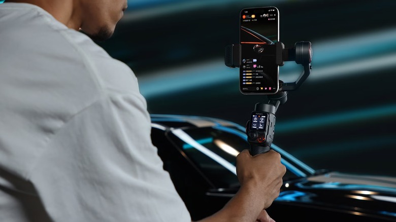 A person filming a car with the Hohem iSteady M7 AI Tracking Smartphone Gimbal.