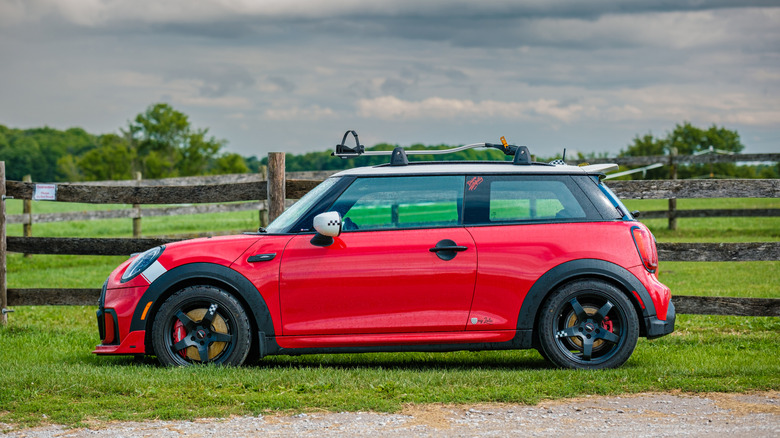 A side profile of a red Mini Cooper hatchback parked in a green environment