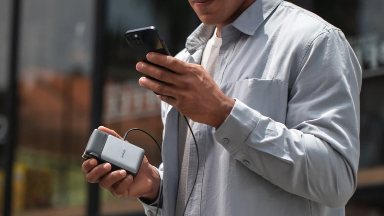 Man holding iPhone in one hand and Anker power bank in the other