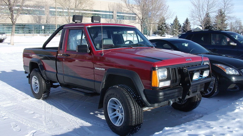 Red Jeep Comanche Eliminator parked on the snow with other vehicles
