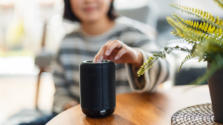A woman interacting with a Bluetooth speaker set on a table in front of her.