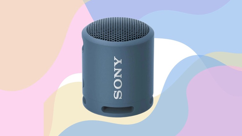 A Sony SRS-XB13 waterproof and dustproof speaker against a multicolored pastel background.