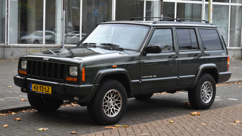 Jeep Cherokee XJ parked on the street, front 3/4 view, very dark green exterior, Dutch plates