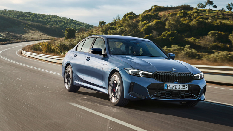 A BMW 330i in blue traveling a road in the mountains