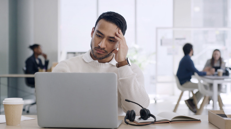 Person sitting at a cafe looking upset at his laptop with a pair of headphones next to him.