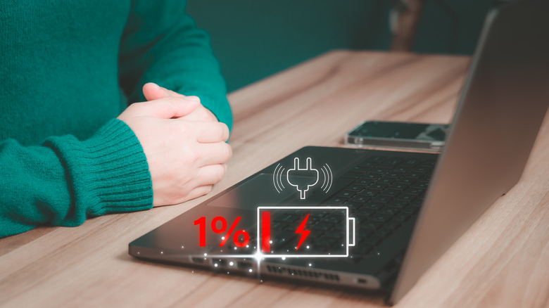 Person crossing their hands in front of a laptop with a low battery symbol displayed on top of it.A
