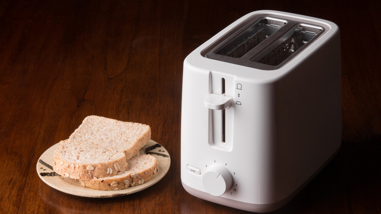 A toaster and plate of bread on a table.