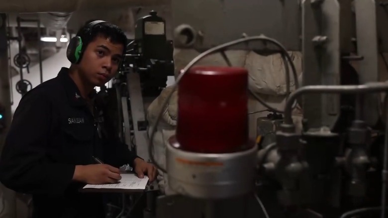 A Navy Machinist's Mate wearing hearing protection while inspecting propulsion equipment
