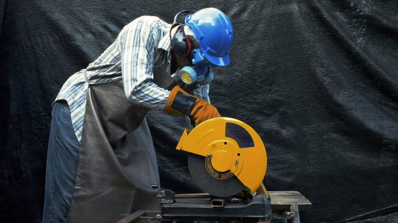 A construction worker cutting through a metal bar with a chop saw