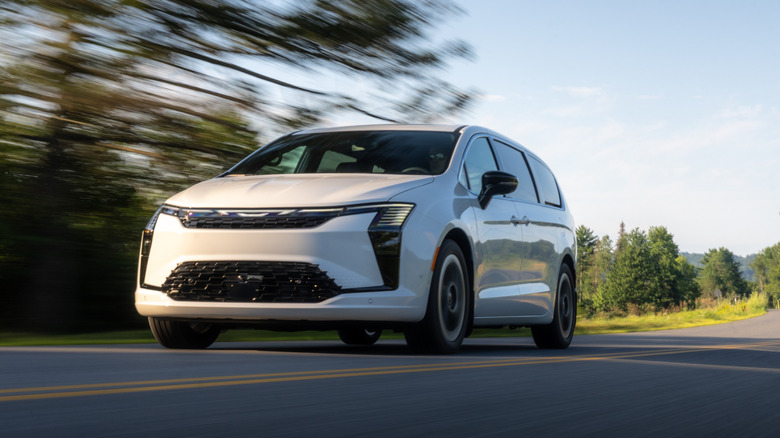A white 2027 Chrysler Pacifica on the move on a rural road, front 3/4 view