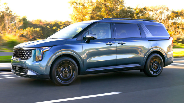 A bluish green 2027 Kia Carnival on the road, side view