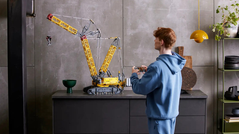 A man operating the Liebherr Crawler Crane LR 13000 LEGO Technic set from his smartphone.