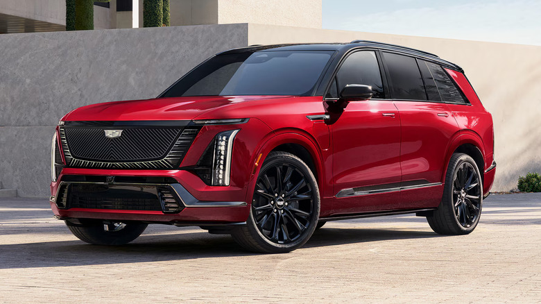 front left view of red Cadillac Vistiq SUV parked on city sidewalk with wall and building behind