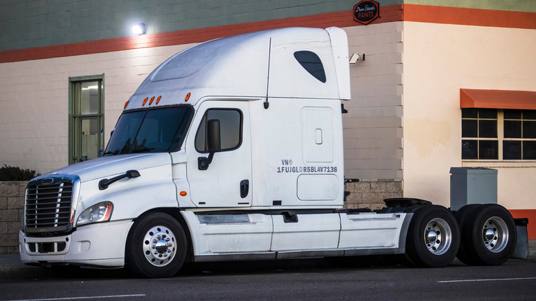 A white freightliner Cascadia next gen rig parked outside a supply depot waiting to be loaded up