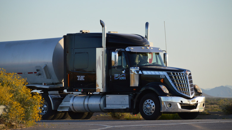 A customized black and silver International Lonestar semi rig traveling on a narrow road