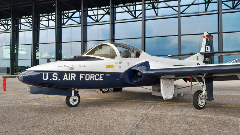 T-37 Tweet aircraft parked in front of glass hangar