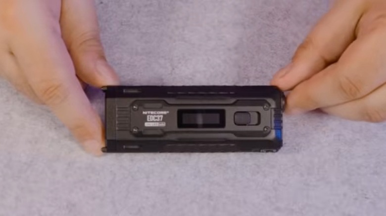 Top-down of hands holding the Nitecore EDC37 flashlight on a gray background.