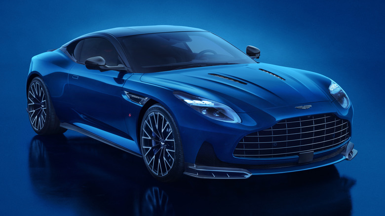 A blue 2026 Aston Martin DB 12 S parked on display with blue futuristic studio background