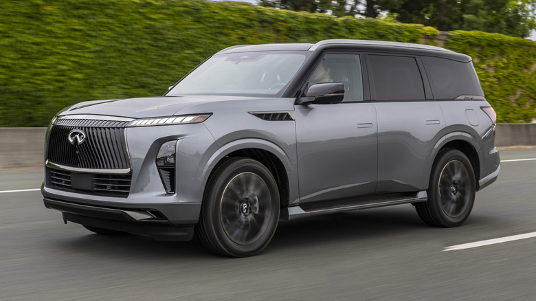 2025 Infiniti QX80 driving on a road with a green hedge on the side