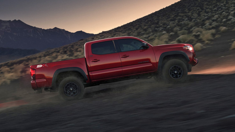 Side view of red Toyota Tacoma pickup on desert trail during evening.