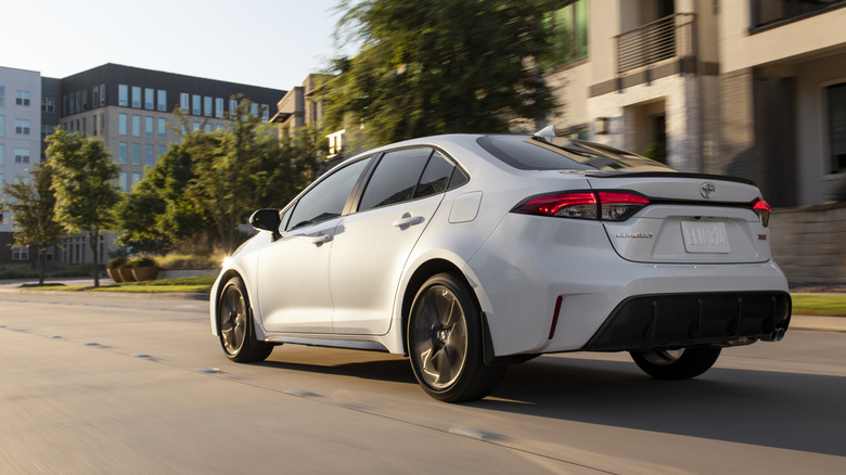 Rear 3/4 view of white Toyota Corolla sedan driving on street.