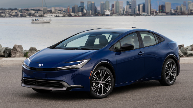 Front 3/4 view of blue Toyota Prius parked in front of harbor.