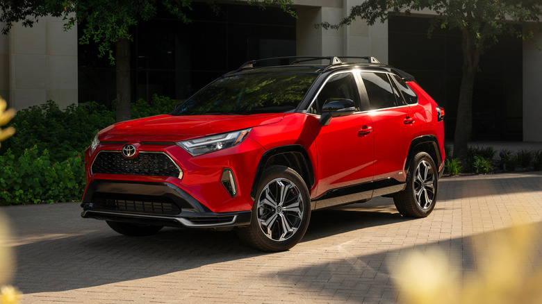 A red 2025 Toyota RAV4 PHEV XSE parked outside a building on a sunny day, front 3/4 view