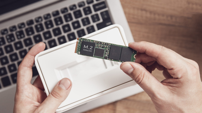 M.2 SSD in hand over a laptop