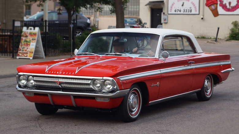 Red 1962 Oldsmobile Jetfire coupe seen from front left driving in a street
