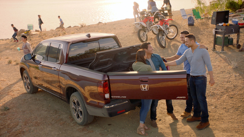 People gather around a red 2017 Honda Ridgeline showing the Dual-Action Tailgate swung open and the In-Bed Trunk open