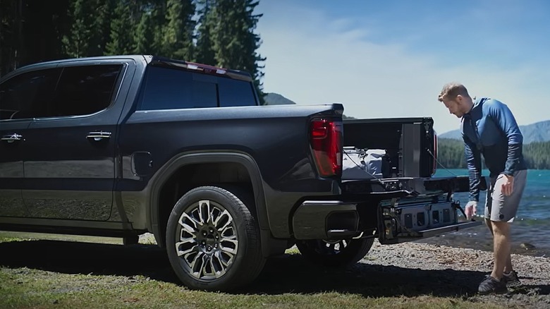 A man opens the MultiPro tailgate on a black GMC Sierra pickup truck by a lake