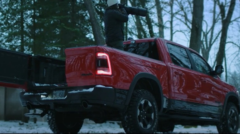A photographer stands in the back of a red Ram 1500 pickup truck with half of the Multifunction Tailgate open