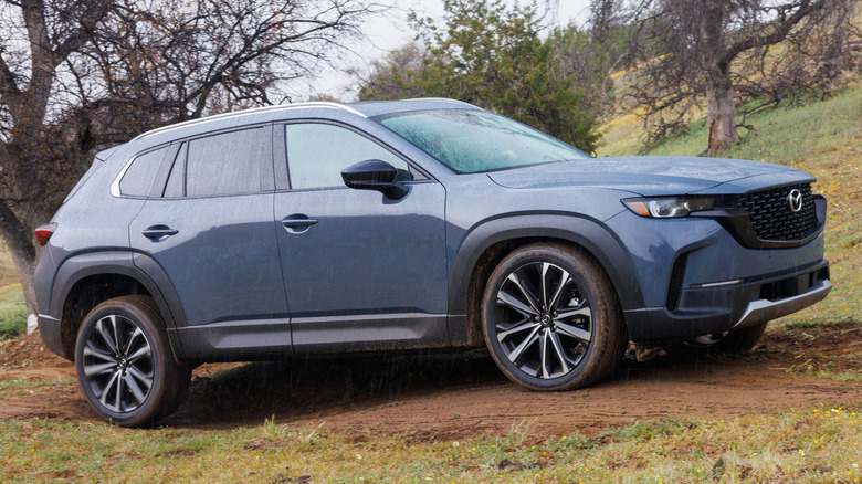 blue 2026 Mazda CX-50 parked in a forest in the rain