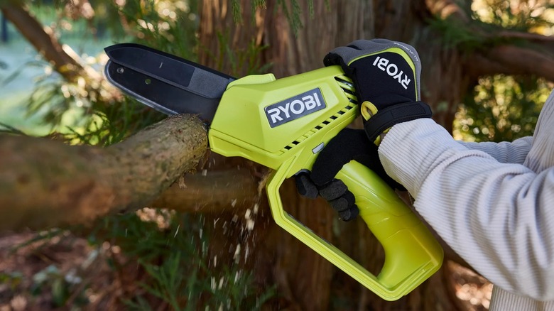 A person using a Ryobi pruning chainsaw on a tree branch.