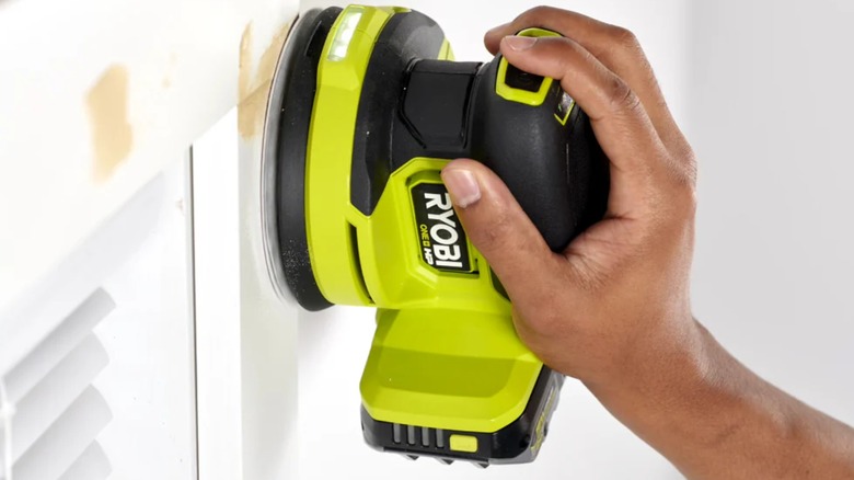 A person using a Ryobi hand sander on wood.