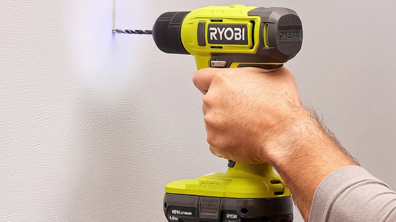 A person using a Ryobi cordless drill on a wall.