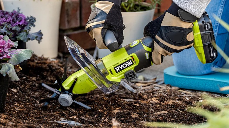 A person using a handheld Ryobi cultivator in soil.